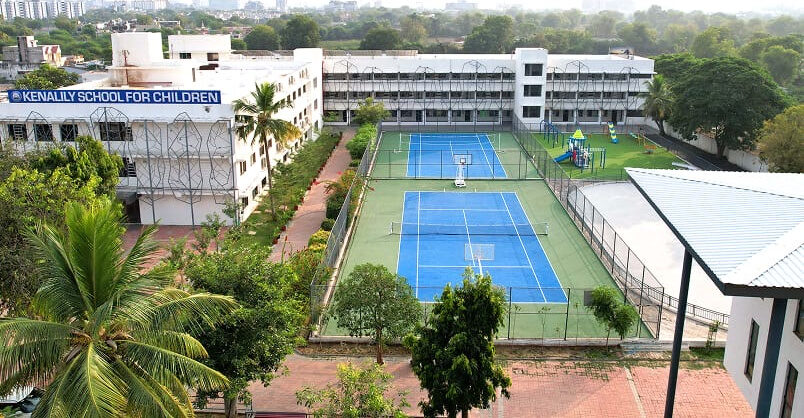 The Kenalily School campus from above: the school buildings, two courts and a playground, with Ahmedabad behind